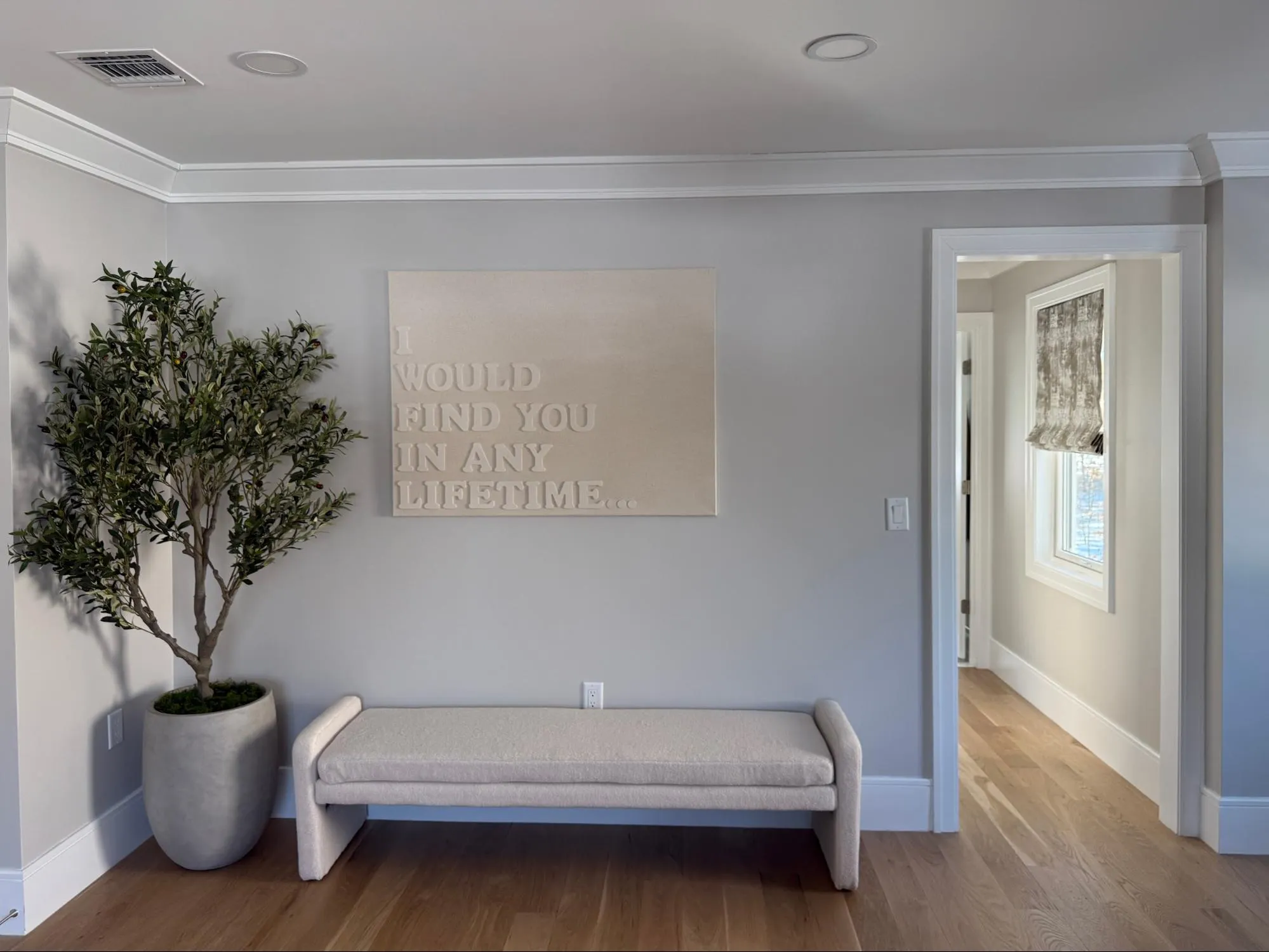 Hallway entryway with upholstered bench, olive tree, and wall art